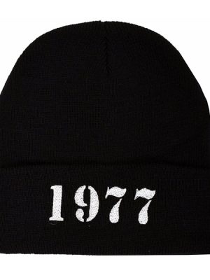 Black knitted punk beanie hat with wide folded cuff featuring bold white 1977 lettering embroidered in a distressed stencil-style font.