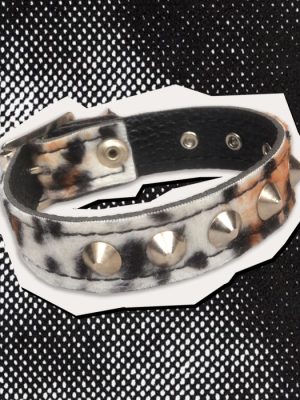 Adjustable leopard print punk wrist cuff featuring distressed grey, black and brown animal print fabric, large silver-coloured cone studs, black inner lining and metal fastening eyelets, photographed against a black and white halftone background.