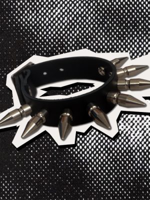Black leather punk wrist cuff featuring long pointed silver-coloured metal spikes arranged around the outside, photographed against a black and white halftone background.