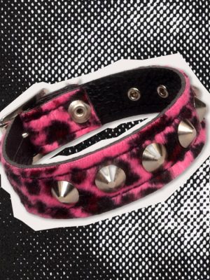 Pink and black leopard print studded wrist cuff featuring four large silver-coloured cone studs, adjustable metal fastening eyelets and black inner lining, displayed against a black and white halftone background.