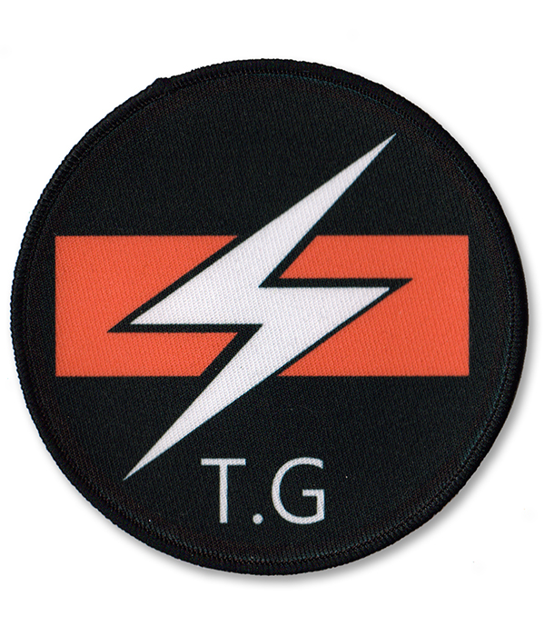 Round Throbbing Gristle sew-on patch with white lightning bolt and orange bar logo on black background.