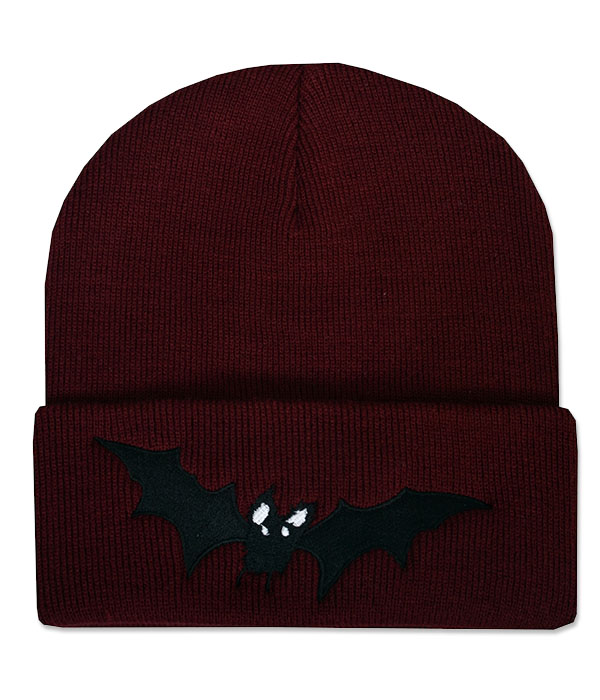 Deep burgundy knitted beanie hat with wide folded cuff featuring a black embroidered vampire bat with outstretched pointed wings and small white eyes.